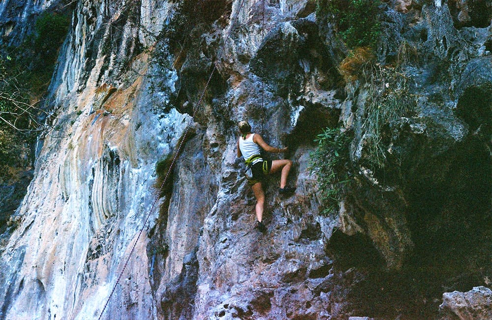 A climber on the limestone at Railay, with bolts in the rock and the beach below