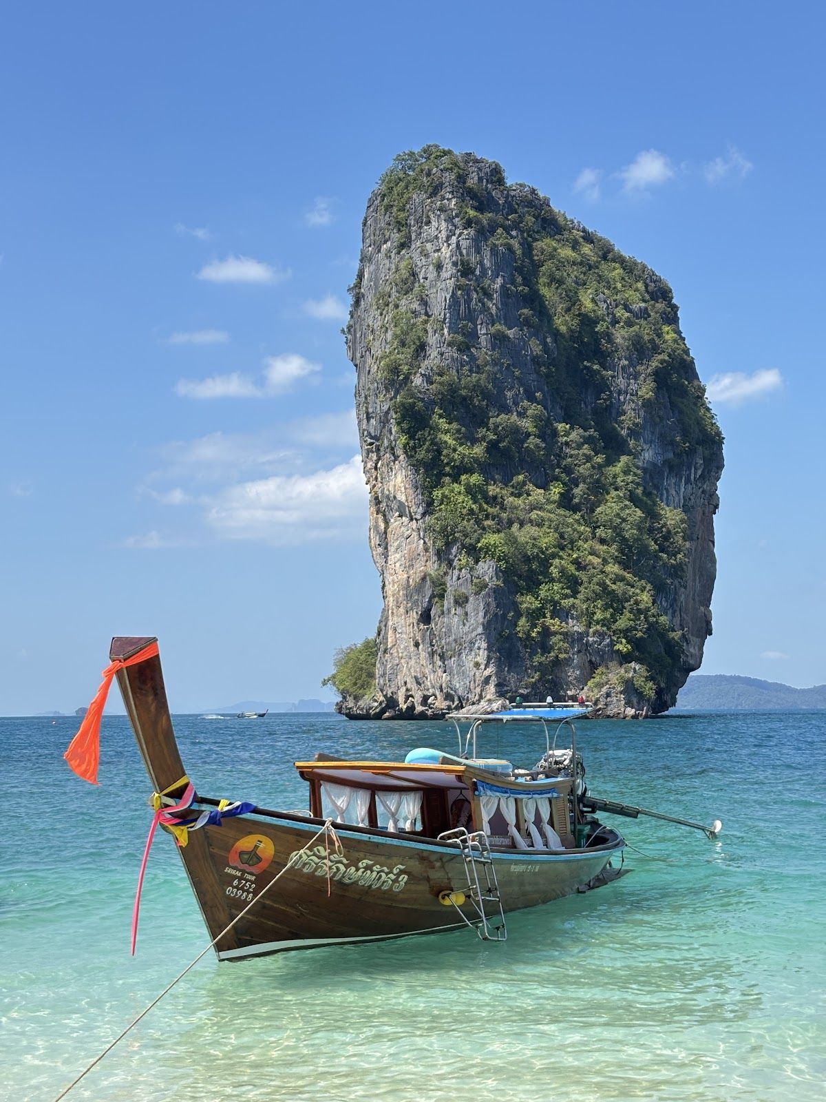 A longtail boat anchored in clear turquoise water off Krabi with a tall limestone karst rising from the sea