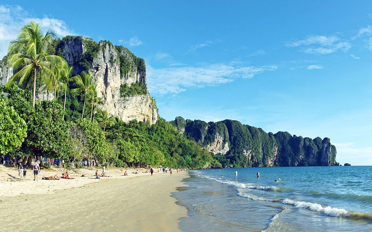 Ao Nang Beach in Krabi with limestone cliffs along the shoreline and people on the sand