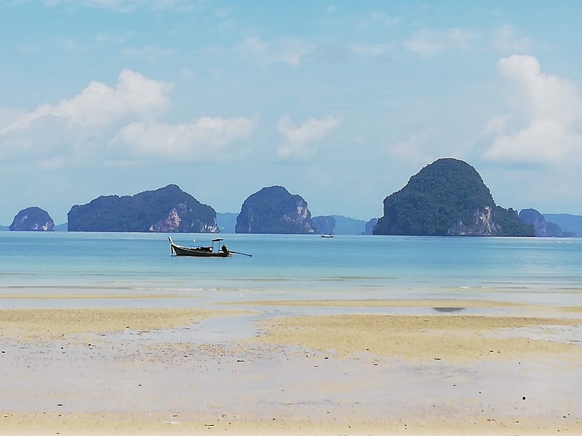 Tubkaek beach faces west toward a cluster of karst islands — the best mainland sunset view in Krabi, and the reason this stretch attracts boutique-tier resorts Tubkaek Beach in Krabi at low tide with a longtail boat and limestone karst islands in the distance