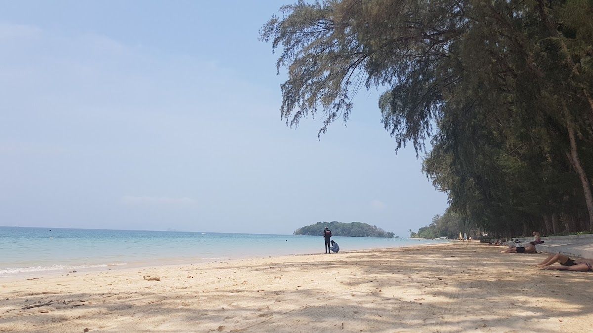 Klong Muang Beach in Krabi, a calm tree-lined shore with pale sand and a small island offshore